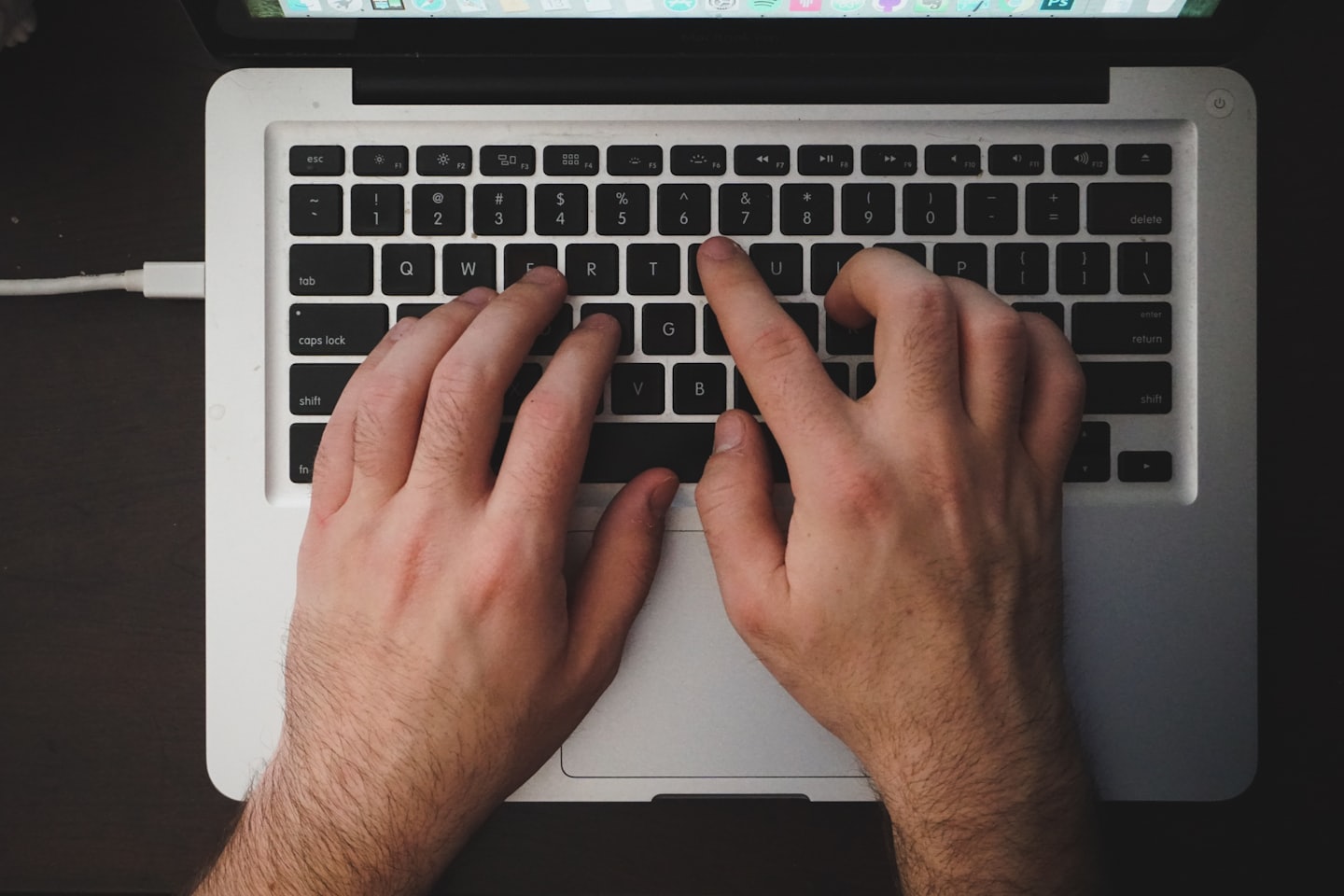 Mani che digitano su una tastiera di laptop con schermo visibile.