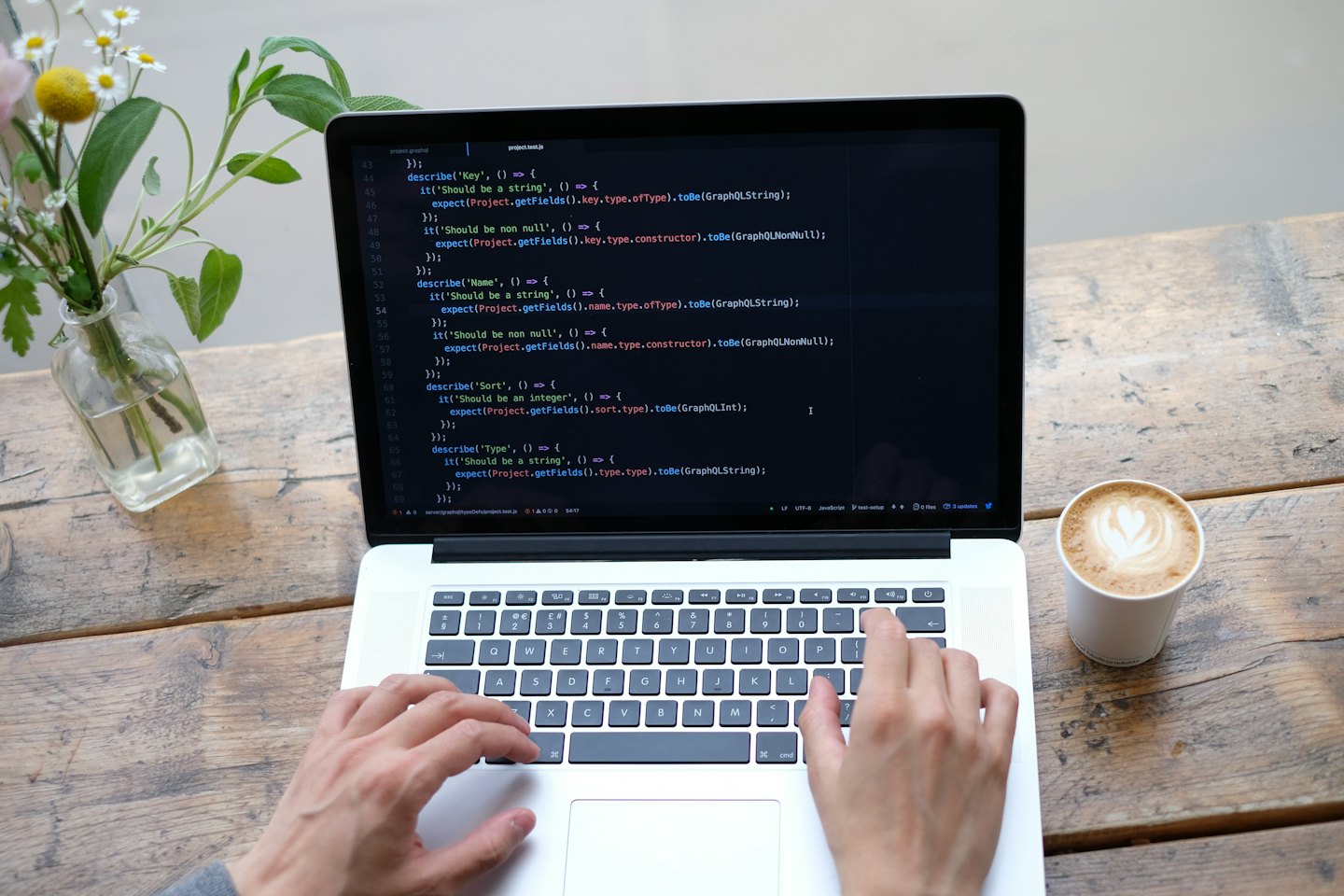 Mani che scrivono codice su un laptop accanto a un caffè.